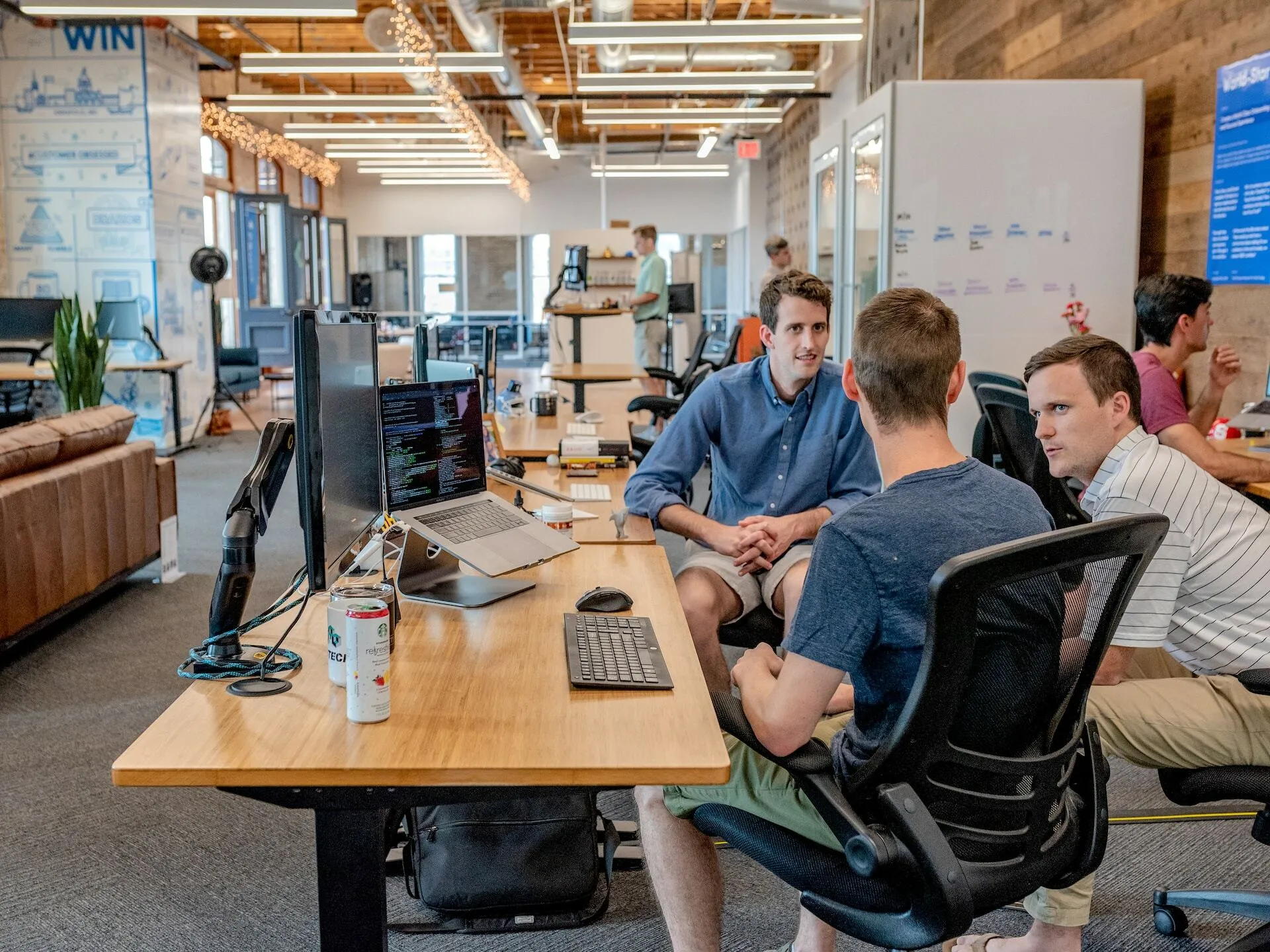 Three men discuss in front of a computer desk