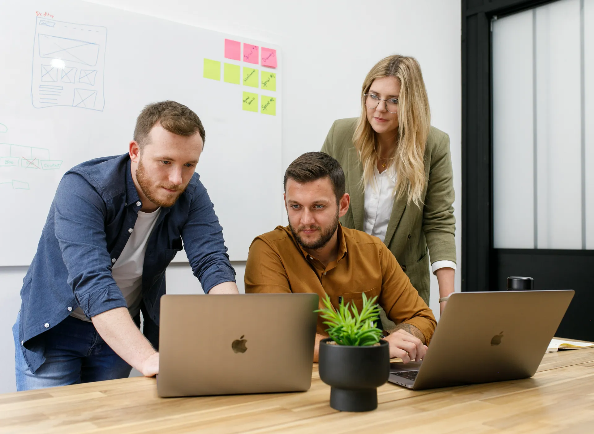 Three people at laptops by a wall of sticky notes
