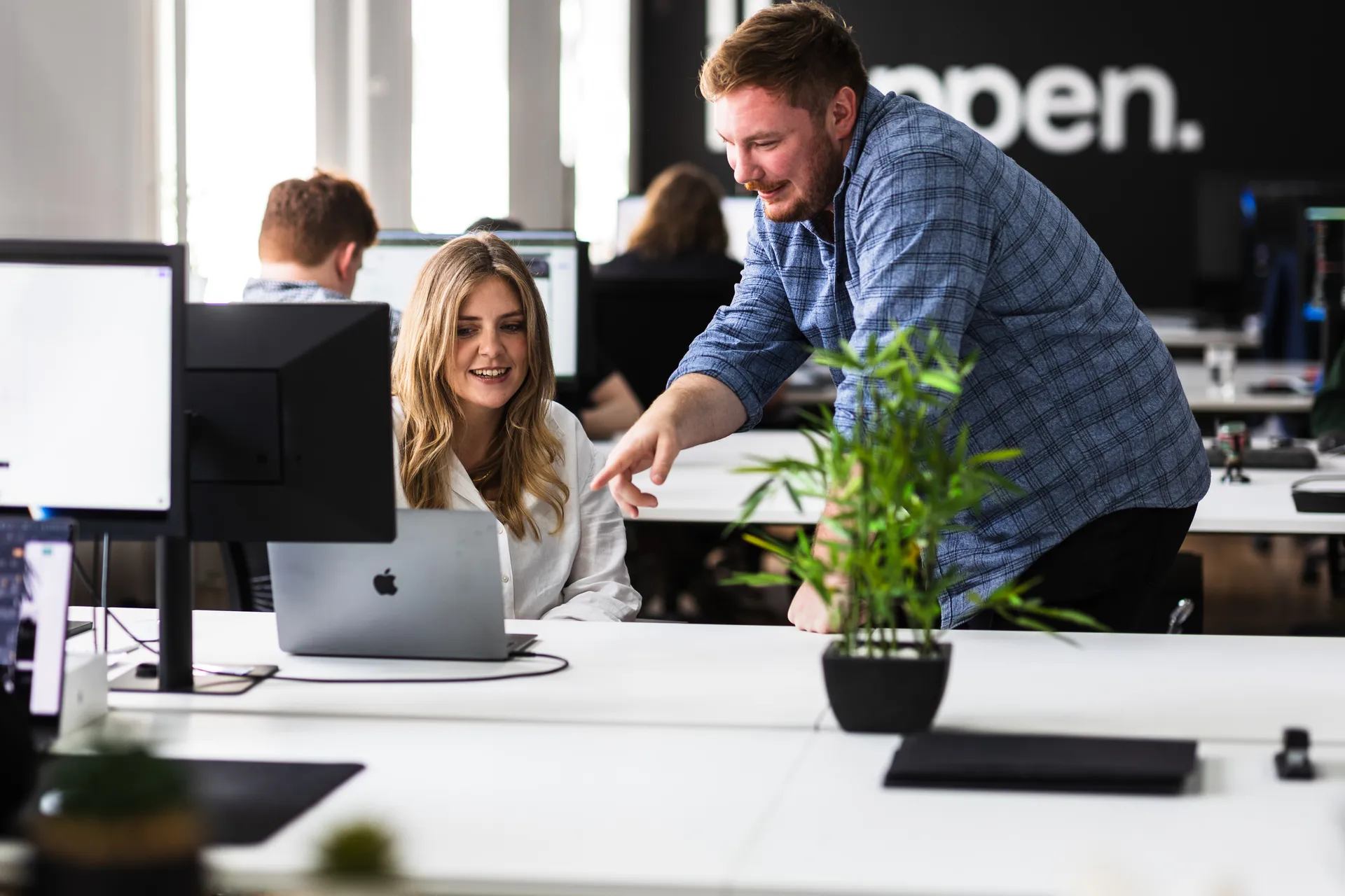 Colleague leaning over to review work on a teammate's laptop