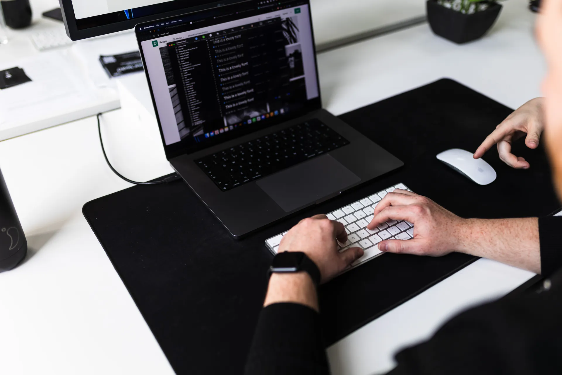 Hands on a laptop keyboard with code, colleague pointing