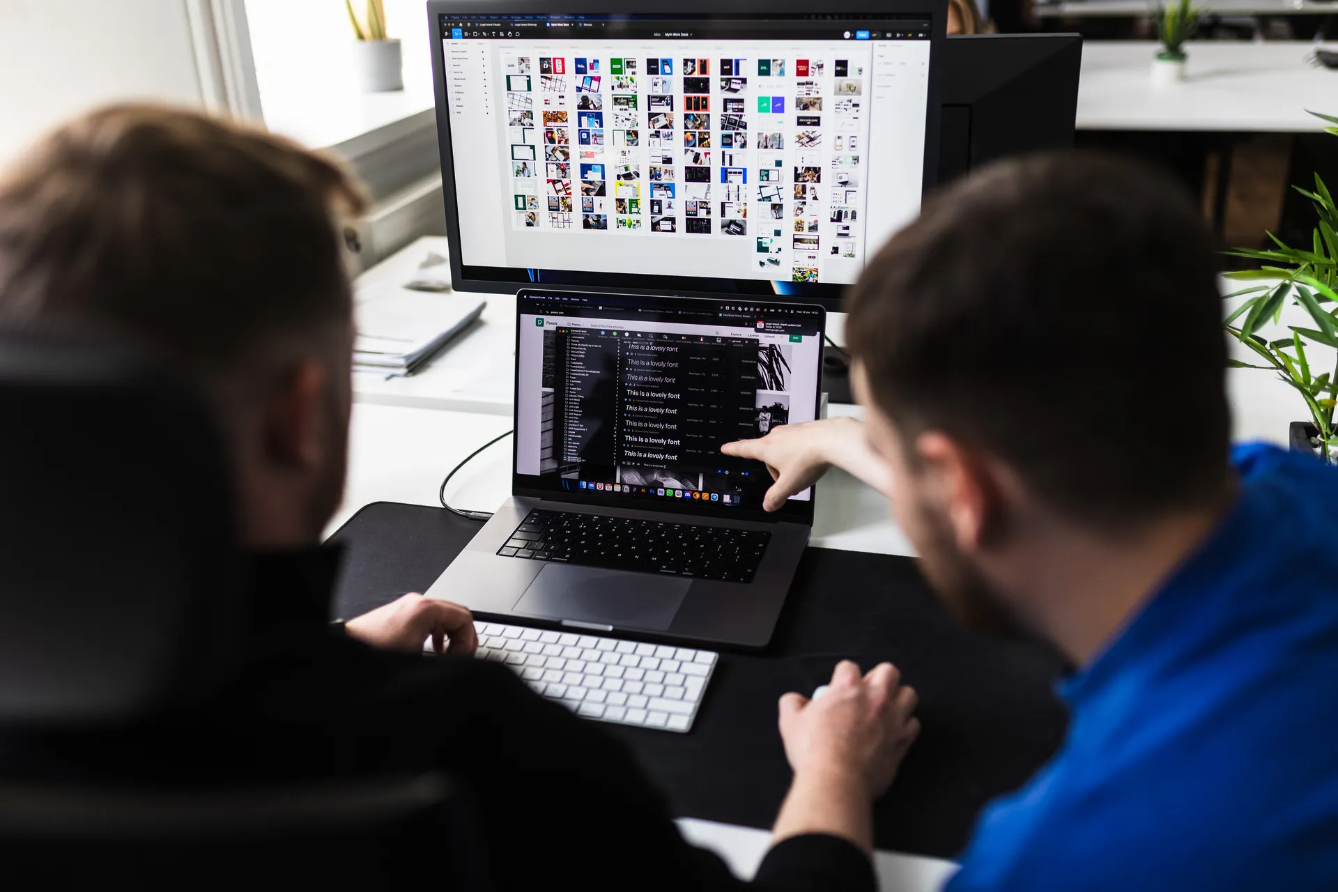 Developer pointing at code on a laptop while a colleague types