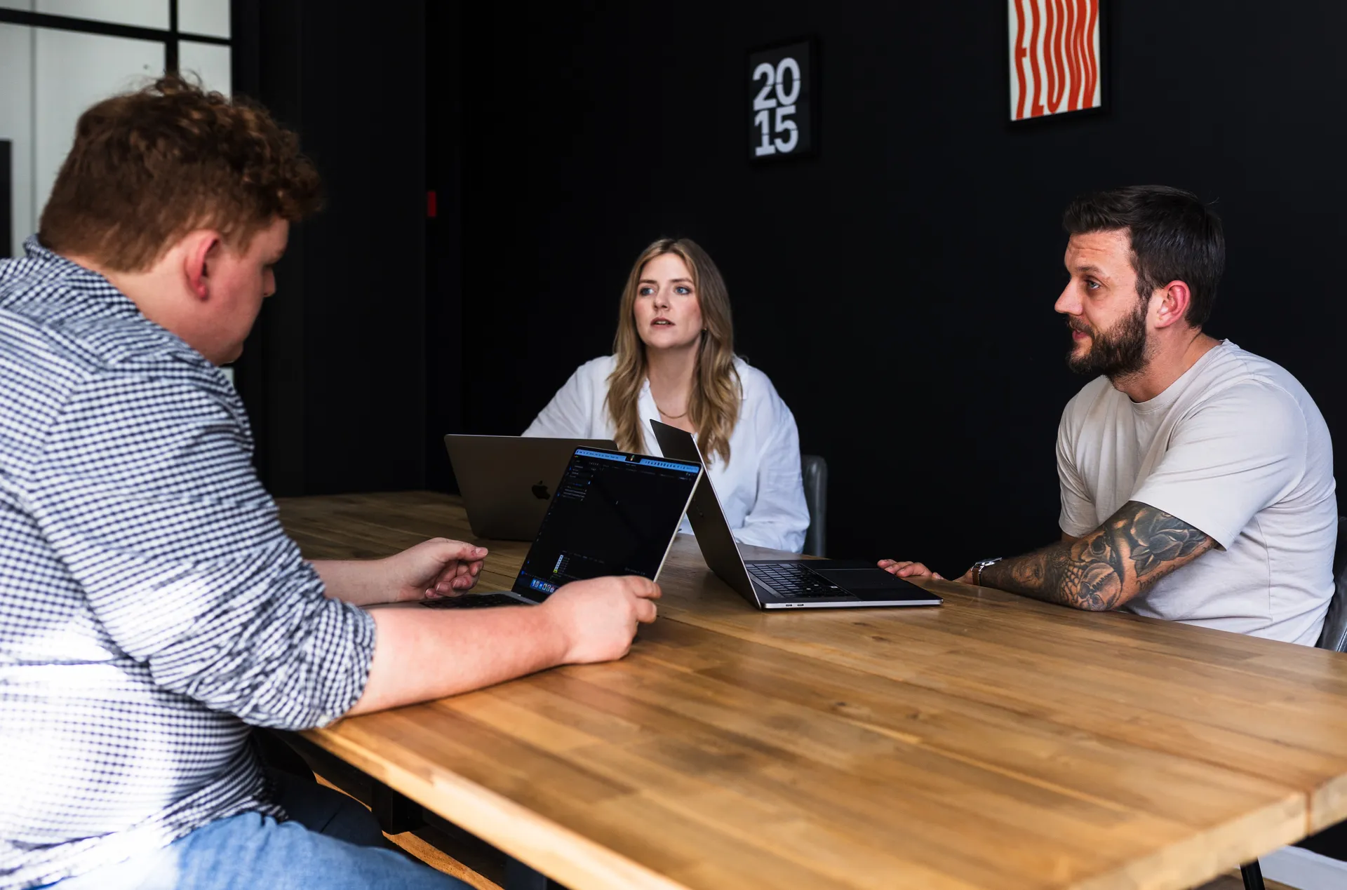 Three people meeting at a wooden table in the dark room with framed prints
